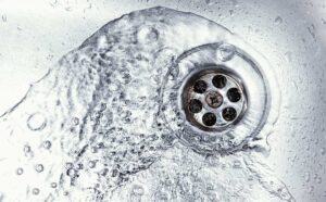 A close-up view of a single faucet with water drops falling into a stainless steel sink at night.