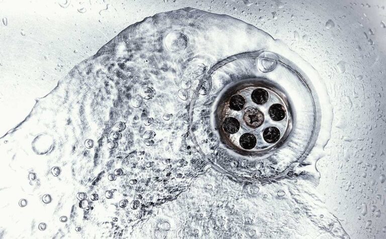 A close-up view of a single faucet with water drops falling into a stainless steel sink at night.