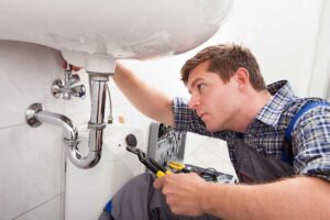 A plumber inspects a leaking toilet in a residential bathroom while using a wrench.