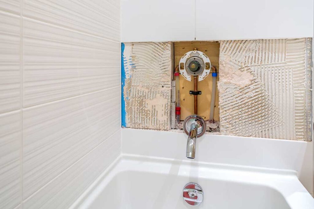 A homeowner checks a water meter while a plumber inspects a leaking toilet and damp bathroom cabinet.
